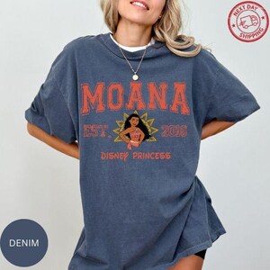A woman wearing a blue t-shirt with the text "Moana" and "Disney Princess" printed on it, along with a graphic of Moana.