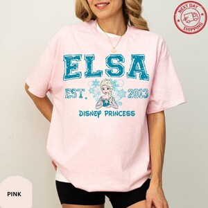 A woman wearing a pink t-shirt with the text "ELSA EST. 2013 DISNEY PRINCESS" printed on it.