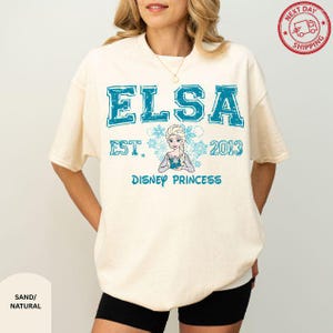 A woman wearing a white t-shirt with a graphic design featuring the character Elsa from the Disney movie Frozen.