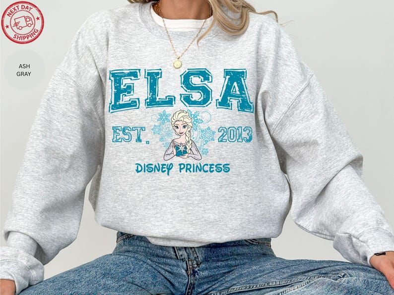 A person wearing a gray sweatshirt with a design featuring the character Elsa from the Disney movie Frozen.