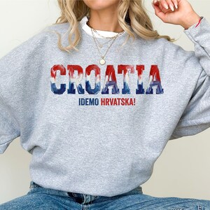 A person wearing a grey sweatshirt with the word "Croatia" printed on it, along with the text "IDEMO HVRATSKA!" printed below.