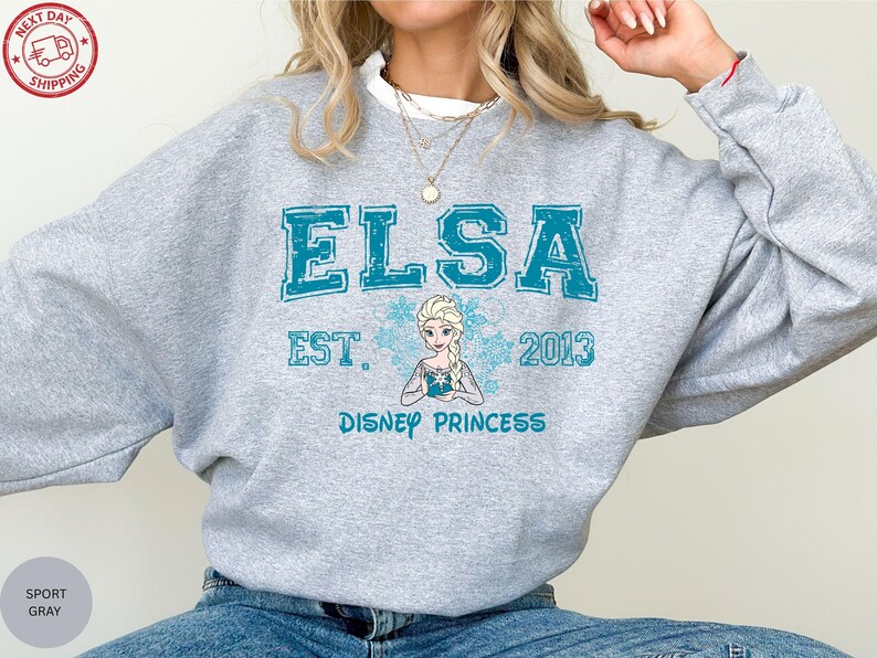 A person wearing a gray sweatshirt with the text "ELSA EST. 2013 DISNEY PRINCESS" printed on it.
