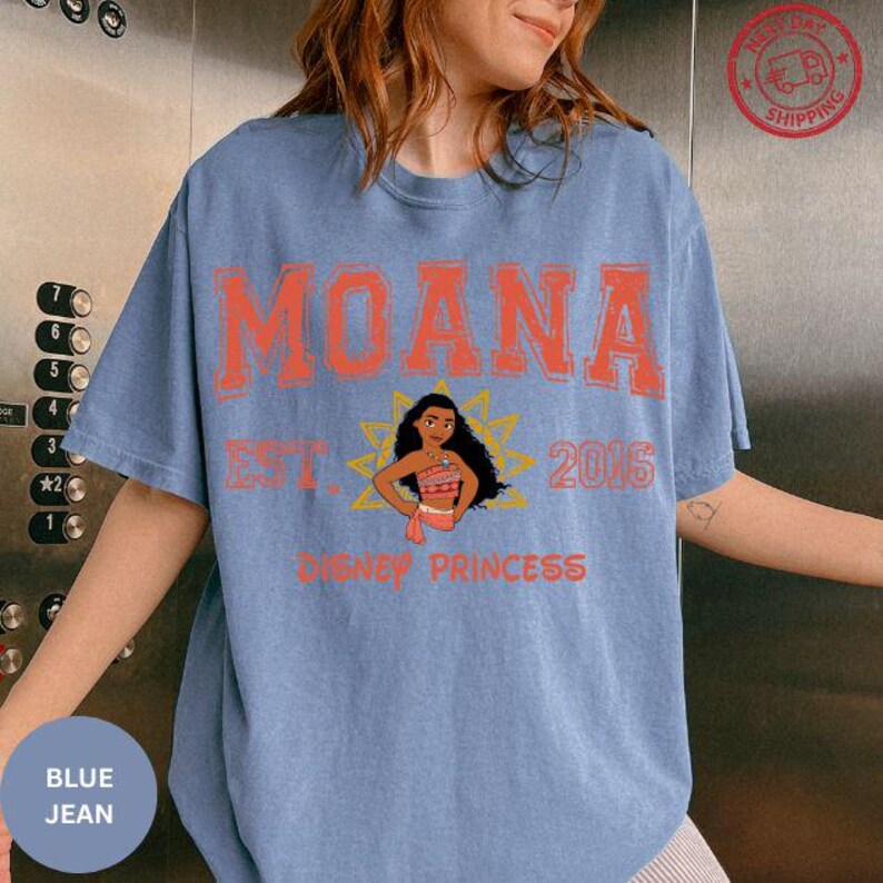 A woman wearing a blue t-shirt with the text "Moana" and "Disney Princess" printed on it.