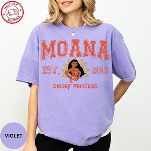 A woman wearing a purple t-shirt with the text "Moana Est. 2016 Disney Princess" printed on it.