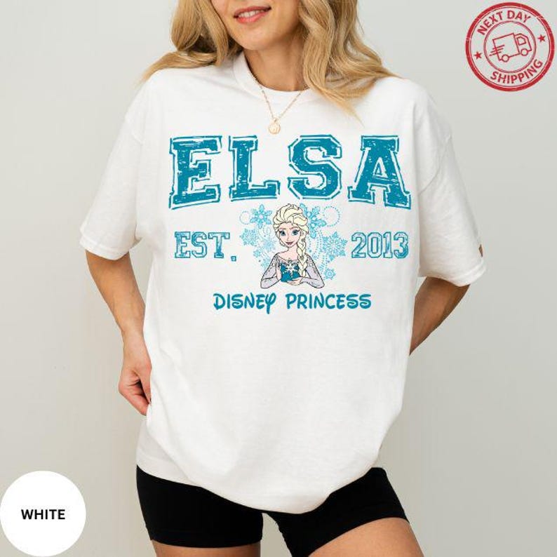 A woman wearing a white t-shirt with the text "ELSA EST. 2013 DISNEY PRINCESS" printed on it, along with a depiction of the Disney princess Elsa.