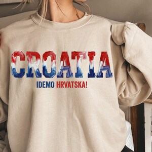 A person wearing a beige sweater with the word "Croatia" printed on it in a stylized font.