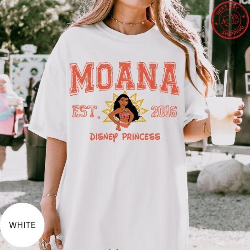 A woman wearing a white t-shirt with the text "Moana Est. 2016 Disney Princess" printed on it, along with an illustration of Moana. She is holding a drink in her hand.