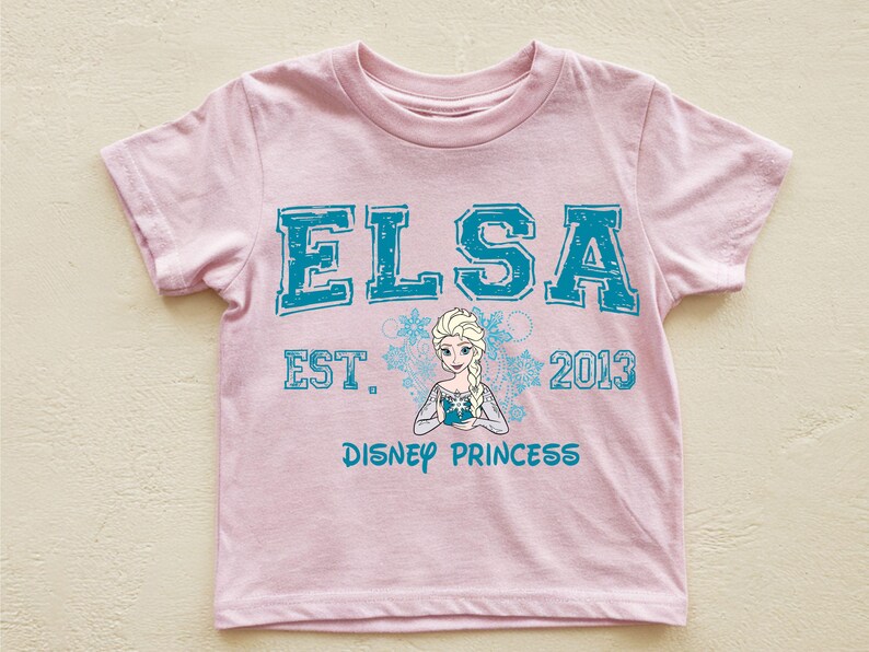A pink t-shirt with the text "ELSA EST. 2013 DISNEY PRINCESS" printed on it, along with a depiction of the Disney princess Elsa.