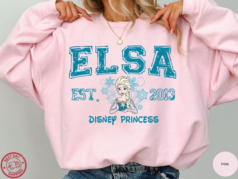 A person wearing a pink sweatshirt with the text "ELSA EST. 2013 DISNEY PRINCESS" printed on it, along with a depiction of the Disney princess Elsa.