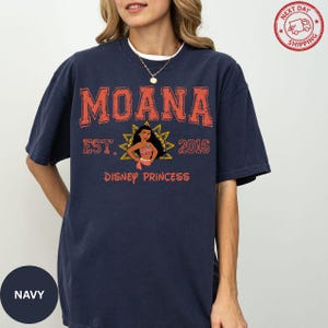A woman wearing a navy blue t-shirt with the text "Moana Est. 2016 Disney Princess" printed on it.