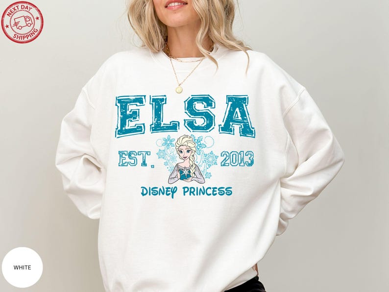 A woman wearing a white sweatshirt with a design featuring the character Elsa from the Disney movie Frozen.