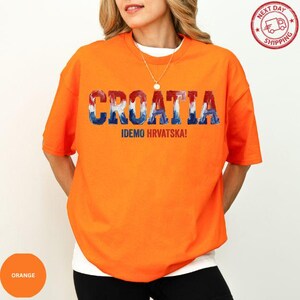 A woman wearing an orange t-shirt with the text "Croatia" and "IDEO HRVATSKA!" printed on it.