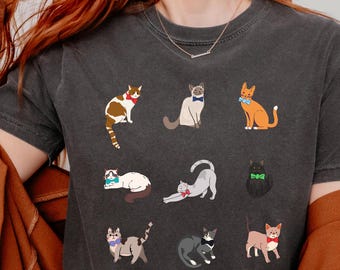 May include: Dark gray t-shirt featuring a collection of illustrated cats in various poses, each adorned with a bow tie or accessory. The word "Pepper" is printed on the top right. The shirt is made of a soft material.