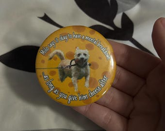 May include: A circular, yellow badge featuring a cartoon dog and the text: "Milo says it's okay to have a mental breakdown...as long as you give him cheese after."