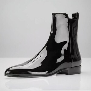 May include: A single, glossy black ankle boot with a pointed toe and a low, rectangular heel. The boot has a pull tab at the back and reflects the surrounding light. The overall style is sleek and modern.