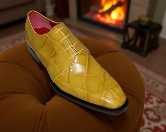 May include: A single yellow leather dress shoe with a textured, quilted pattern. The shoe has a black sole, yellow laces, and a pink interior. The shoe is displayed on a brown ottoman, with a fireplace in the background.