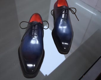 May include: A pair of two-tone dress shoes. The shoes transition from a deep navy blue to black at the toe, with a red interior. The shoes have a glossy finish, laces, and a classic Oxford design.