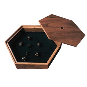 May include: Hexagonal wooden dice box with a dark green felt interior and a matching wooden lid. The box contains several black dice with gold numbering. The lid is partially open, revealing the dice inside.