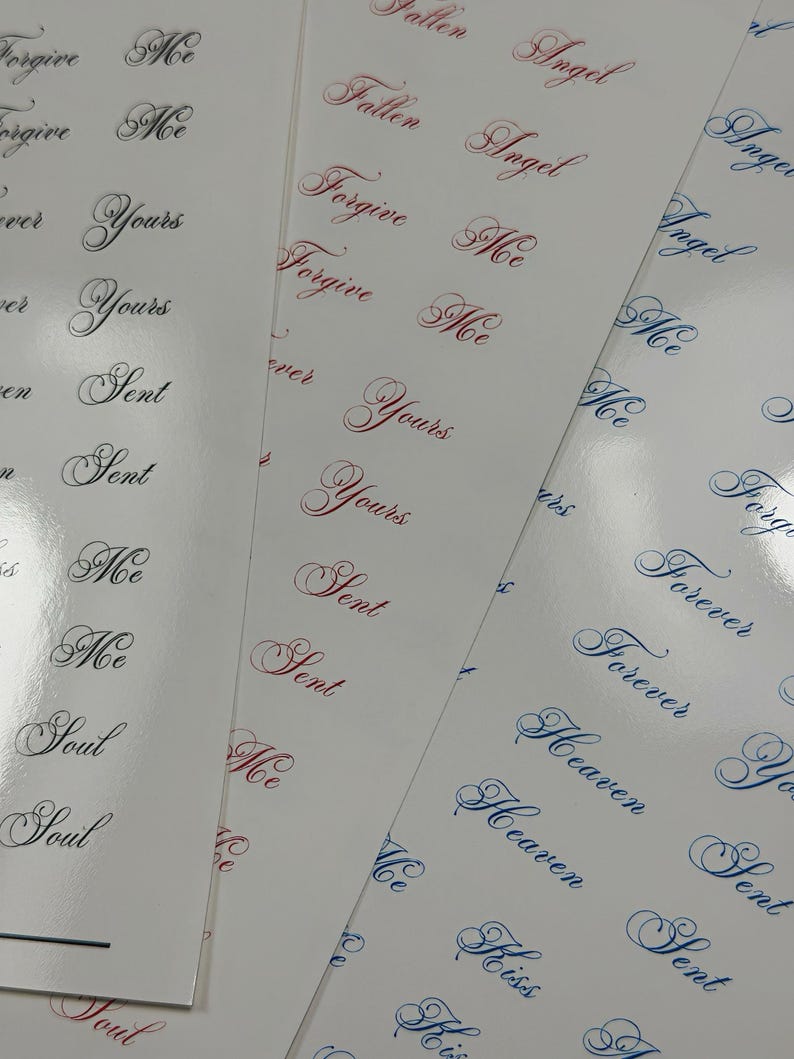 May include: Three sheets of white adhesive stickers featuring repeating words in elegant cursive script. The text includes Forgive Me, Yours, Sent, Me, Soul, Fallen Angel, Forever, Heaven, and Kiss, printed in black, red, and blue ink colors.