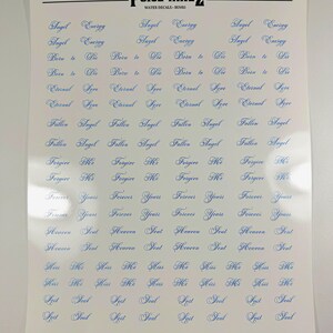 May include: A white sheet of water nail decals by POISE NAILZ featuring multiple rows of blue cursive text including phrases like Angel Energy, Born to Die, Eternal Love, Fallen Angel, Forgive Me, Forever Yours, Heaven Sent, Kiss Me, and Lost Soul.