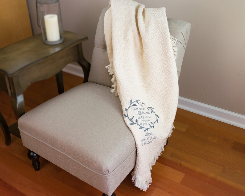 May include: A cream-colored throw blanket with a fringe border and a blue embroidered wreath with the text "that we are all the more HOPE TO BE now that you are to you" and "Love, Jack & Julie 1.10.2015".