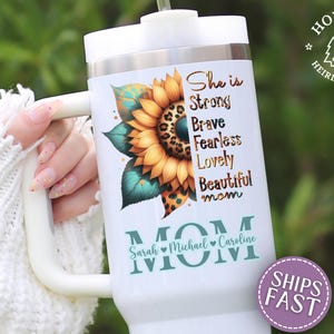 May include: White insulated tumbler featuring a sunflower design with the words "She is Strong Brave Fearless Lovely Beautiful mom." The tumbler also includes the names Sarah, Michael, and Caroline. A purple sticker reads "Ships Fast."