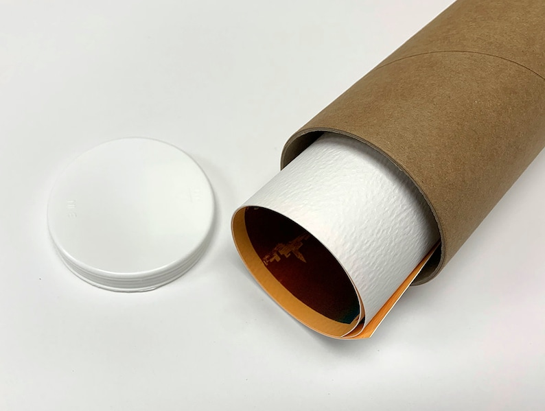 May include: A brown cardboard tube with a white lid. The tube is partially unrolled, revealing a rolled-up poster with orange, red, and green colors.