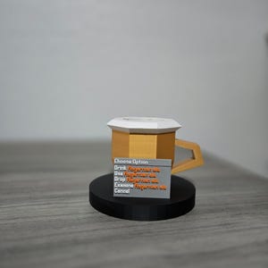 May include: A gold-coloured, geometric mug with a white top and a black base. A small grey rectangle displays the text "Choose Option" and other lines of text in orange. The mug has a unique handle design.
