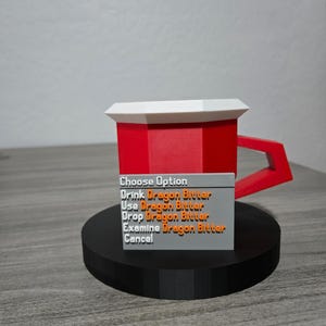 May include: A red and white mug with a geometric design, featuring a handle and a base. A grey rectangular sign displays the text "Choose Option" and several options related to "Dragon Bitter". The mug is on a black circular base.