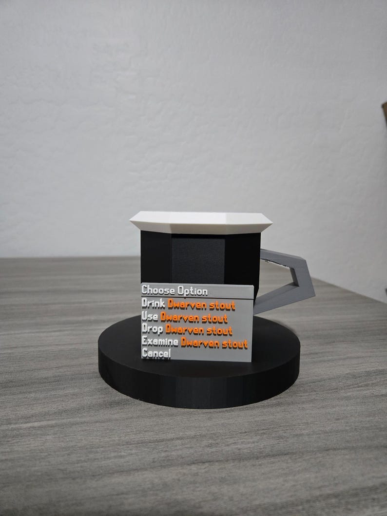 May include: A 3D-printed mug with a black body, white top, and grey handle, on a black circular base. A rectangular sign displays the text "Choose Option" and options related to "Dwarven stout".