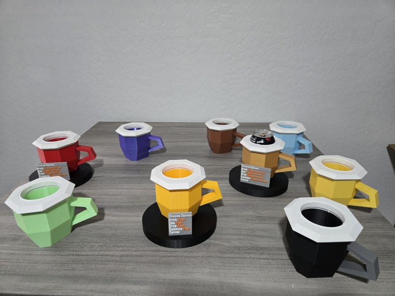 May include: A selection of colourful, geometric paper coffee cups with white rims and handles. The cups are in various colours, including red, green, yellow, blue, brown, and black. Some cups have a black base.