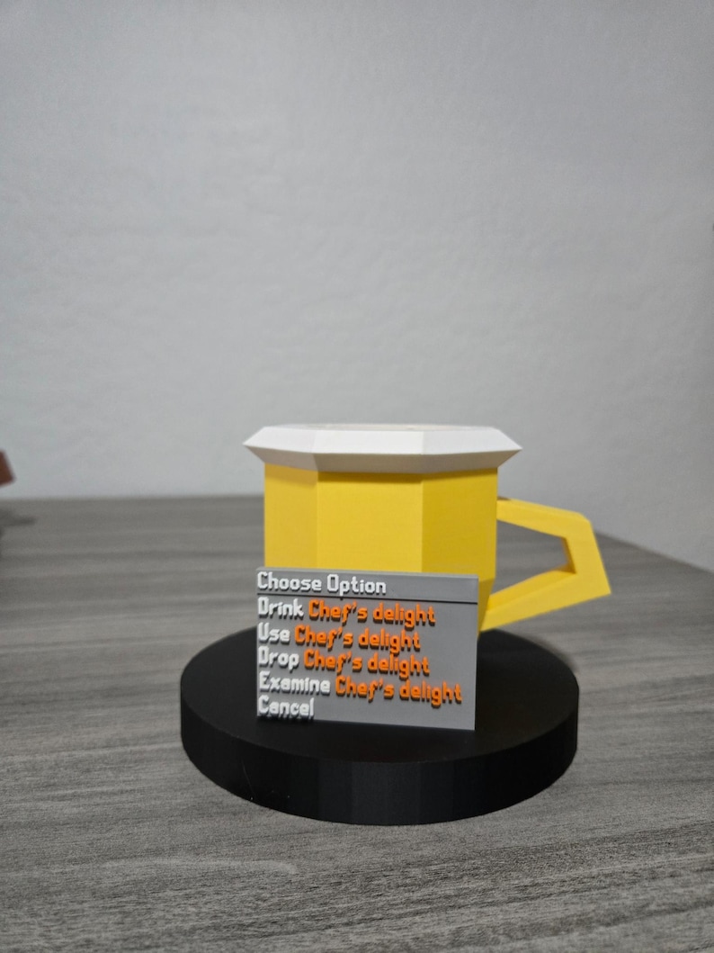 May include: A 3D-printed yellow mug with a white top and a rectangular handle. A small grey sign in front of the mug displays the text "Choose Option" and several options related to "Chef's delight."