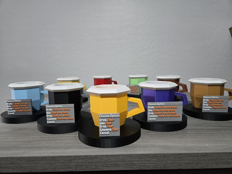 May include: A display of multi-coloured, geometric mugs with white lids and black bases. Each mug is a different colour, such as blue, yellow, black, purple, and brown. Small signs with text are in front of each mug.
