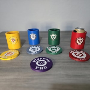 May include: A collection of cylindrical beverage holders and circular coasters in yellow, blue, green, red, and purple. Each item features a printed logo with text including Revive Soda, Speed Cola, Jugger-Nog Soda, and Flopper PHD.