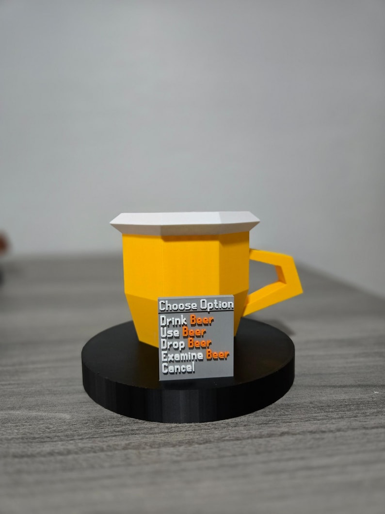 May include: A yellow polygonal beer mug with a white top and a handle, on a black circular base. A small grey rectangle displays the text "Choose Option" and beer-related actions. The mug is a 3D-printed item.