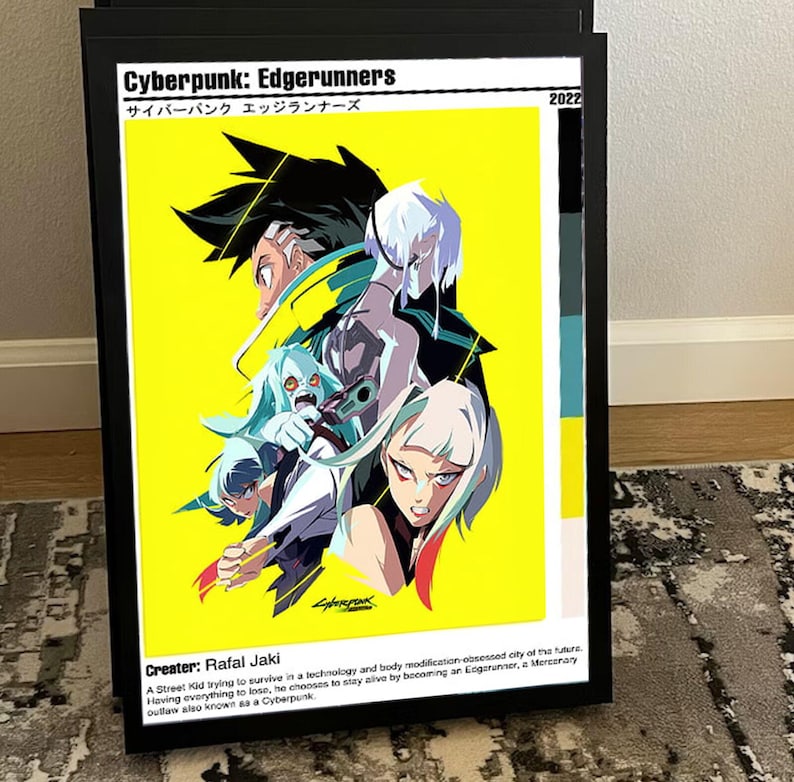 K&ouml;nnte beinhalten: Gerahmtes Poster f&uuml;r den Anime "Cyberpunk: Edgerunners" mit gelbem Hintergrund. Die Illustration zeigt Charaktere in dynamischer Pose, mit Text in Englisch und Japanisch. Das Poster enth&auml;lt das Jahr 2022 und den Namen des Sch&ouml;pfers, Rafal Jaki.