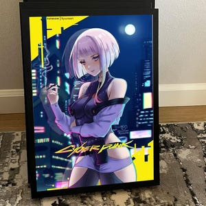 K&ouml;nnte beinhalten: Gerahmter Druck mit einer digitalen Illustration einer Frau mit kurzen, hellvioletten Haaren, vor einer futuristischen Stadtkulisse. Das Kunstwerk enth&auml;lt den Text "CYBERPUNK" und "PATREON Ryuuneart". Die Farbpalette wird von Blau, Lila und Gelb dominiert.