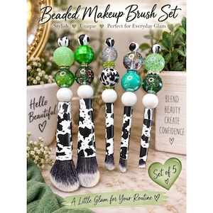 May include: A set of five makeup brushes with handles featuring a black and white cow print pattern. Each brush handle is topped with a stack of decorative beads in shades of green, white, black, and silver, including glitter and marbled finishes.