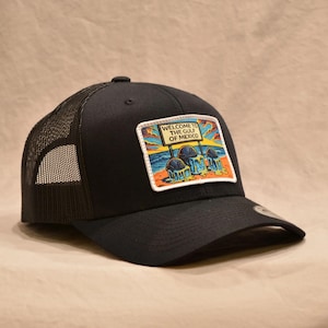May include: Black trucker hat with a mesh back and a curved brim. The front features a rectangular patch with the text "WELCOME TO THE GULF OF MEXICO" above a colorful graphic of melting ice cream cones.