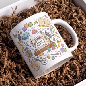 Puede incluir: Una taza de cerámica blanca con un asa negra y el texto "But First, Coffee" en negro, con una fuente de estilo manuscrito. La taza está sobre una superficie blanca.