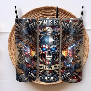 Puede incluir: Un vaso cilíndrico con pajita que presenta un gráfico de una calavera con el patrón de la bandera estadounidense, ojos azules brillantes, un águila calva, hachas cruzadas y el texto Freedom Is Earned, United We Stand y Liberty Never Yields.