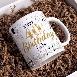 May include: White ceramic mug with "Happy 40th Birthday Katie" in gold glitter script. The mug features black and gold celebratory graphics, including balloons, a party hat, and a cake. The mug is nestled in brown paper shred.