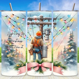 Könnte beinhalten: Ein Edelstahlbecher mit einer Winterszene, die einen Arbeiter an einem Strommast, Lichterketten und den Text "Lighting Up Christmas One Pole at a Time" zeigt. Das Design umfasst eine rosa Schleife und Tannenzweige.