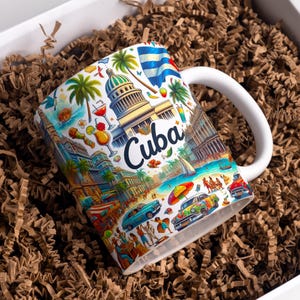 May include: White ceramic mug with a colorful illustration of Cuba, featuring landmarks, palm trees, classic cars, and the word "Cuba". The mug has a white handle and is set in a box with brown packing material.