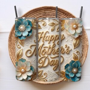 Può includere: Tre bicchieri bianchi con cannucce nere, con disegni floreali in rilievo e la scritta "Happy Mother's Day" in oro. I bicchieri sono adornati con fiori color verde acqua e crema e foglie dorate, appoggiati su un vassoio intrecciato.