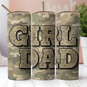 May include: A camouflage-patterned tumbler with the words "GIRL DAD" in a cracked, textured font. The tumbler has a silver straw and lid. The design is in shades of green, brown, and tan.