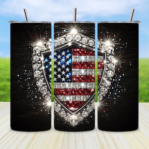 May include: A set of three stainless steel tumblers with a patriotic design. The design features the American flag within a diamond-encrusted shield, set against a black textured background. Each tumbler has a silver straw.