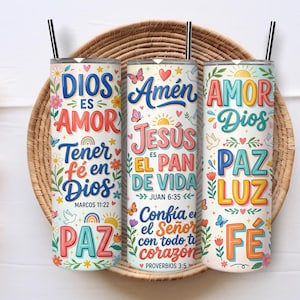 Peut inclure: Trois gobelets cylindriques en métal avec des pailles noires, chacun présentant un fond blanc décoré de motifs floraux colorés, d'arcs-en-ciel et de textes religieux en espagnol incluant des phrases comme Dios es Amor, Jesús es el Pan de Vida et Fe.