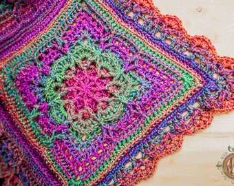 Könnte beinhalten: Eine farbenfrohe, handgefertigte Häkeldecke mit quadratischem Design. Die Decke zeigt ein zentrales Blumenmuster in Rosa und Grün, umgeben von aufwendiger Häkelarbeit in Regenbogenfarben. Die Ränder haben einen gewellten Rand.