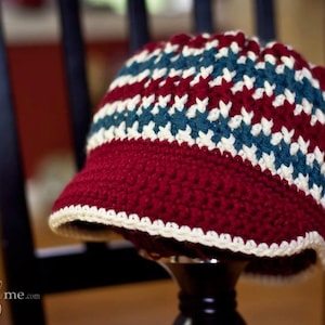 Könnte beinhalten: Eine gehäkelte Mütze in den Farben Rot, Weiß und Blau. Die Mütze hat einen breiten Rand und ein strukturiertes Design.